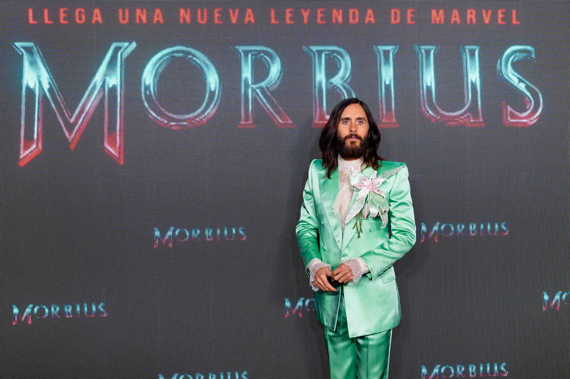 Jared Leto poses at the Madrid promotional showing of Morbius. Leto is wearing a lime green suit in front of a Morbius promotional backdrop in Spanish.