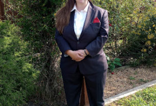 A woman wearing a suit smiles standing in a garden