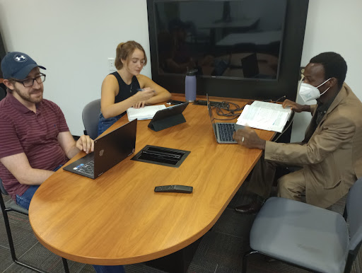 Three students sit at a table with laptops and notebooks