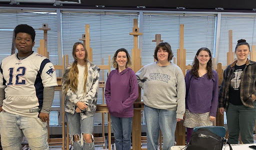 Members of the art club posing together in front of canvases.