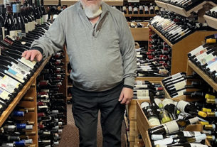 A photo of Bill Curtis standing alongside some of his collected wine bottles.