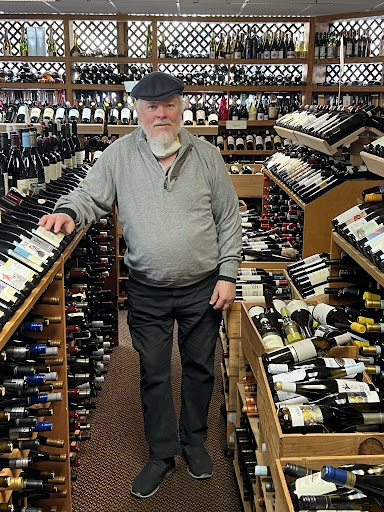 A photo of Bill Curtis standing alongside some of his collected wine bottles.