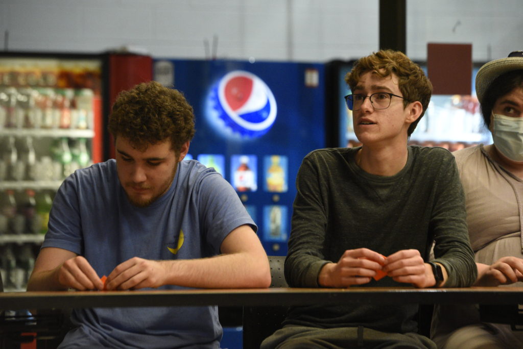 Two male students fold paper at a long table