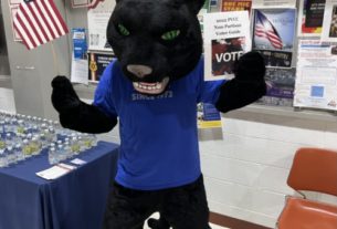 Pounce the Panther, the college mascot is posing with an American flag in his right hand and a voter guide in his left hand