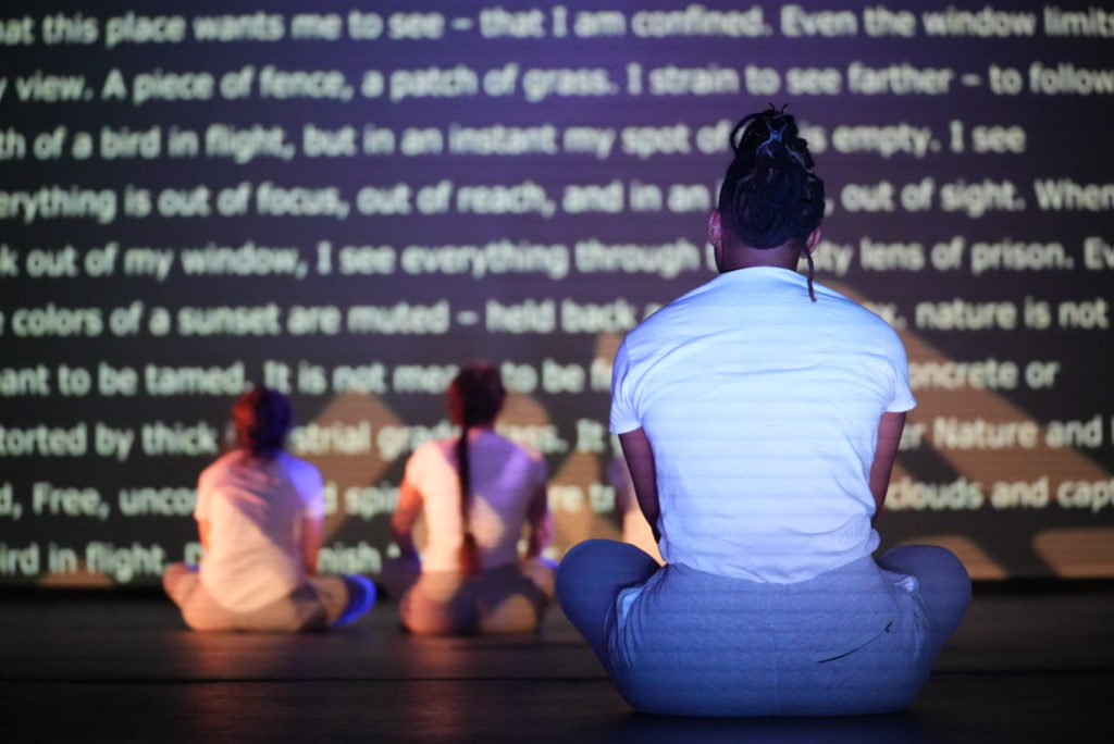 performers sit and read the writing projected on the wall