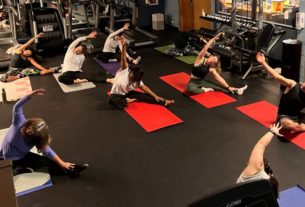 people sit on yoga mats in the fitness center with their arms stretched over their heads