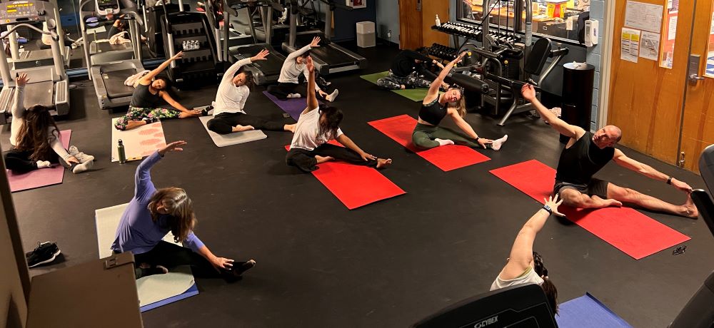 people sit on yoga mats in the fitness center with their arms stretched over their heads