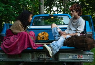 A young woman and young man sit in the back of a pickup truck facing each other