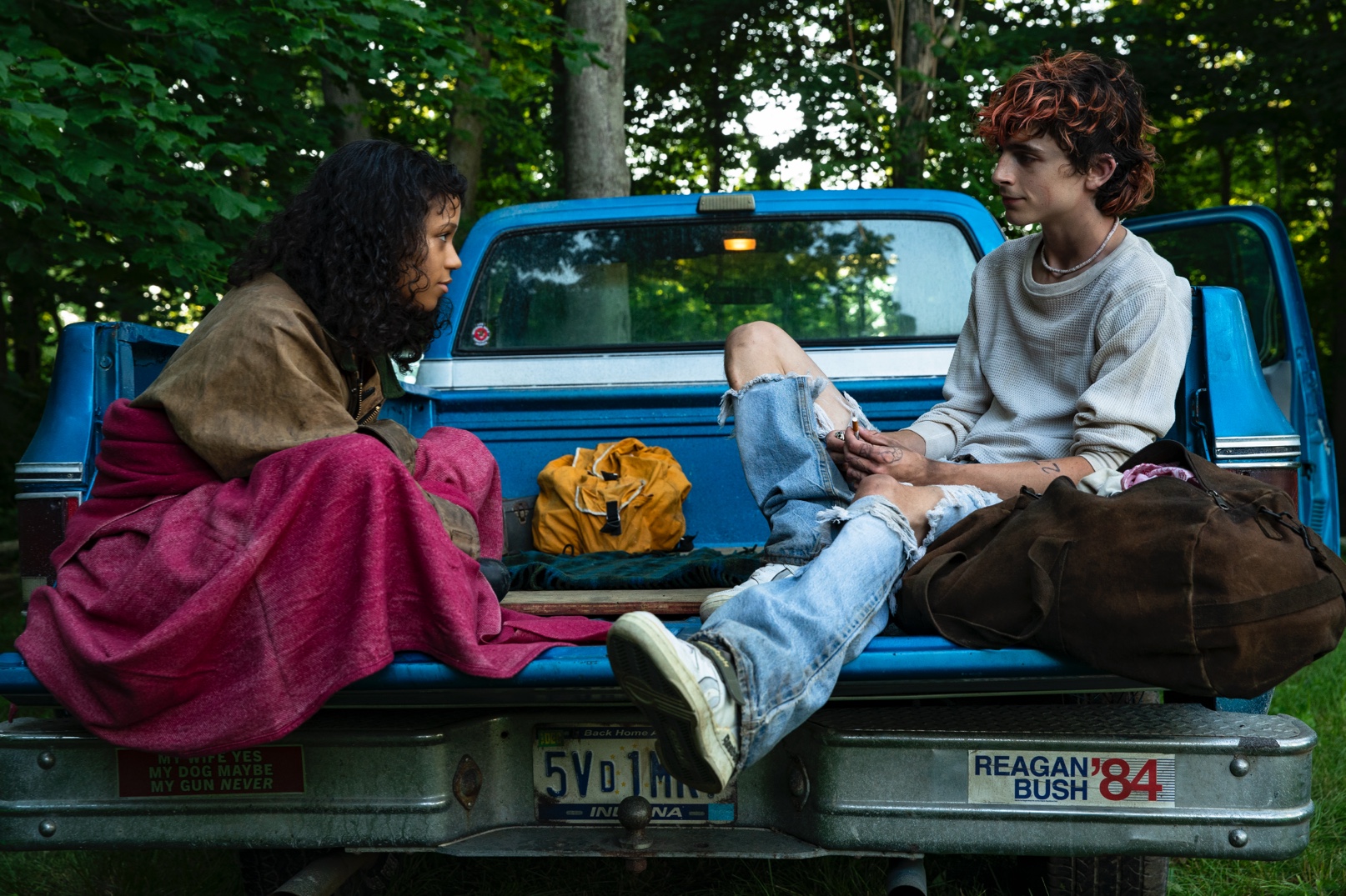 A young woman and young man sit in the back of a pickup truck facing each other