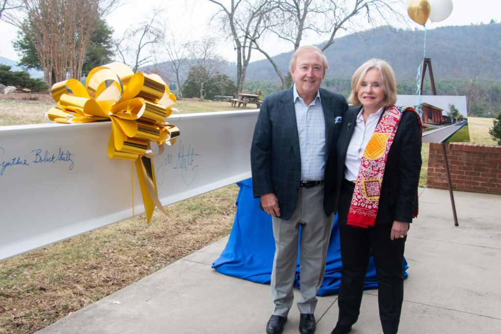 A man and woman pose next to a white metal beam with signatures on it