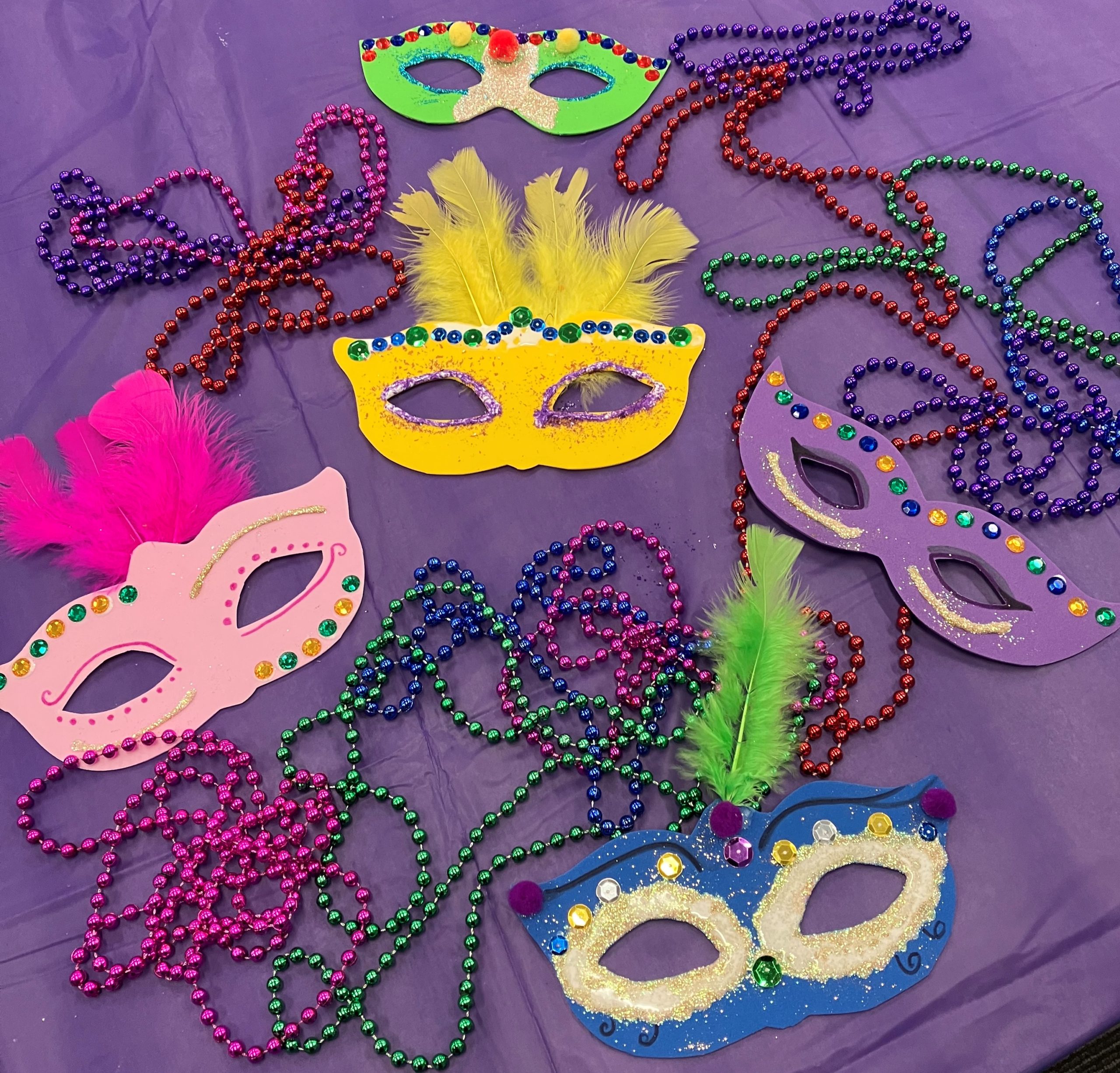 Colorful paper masks and Mardi Gras beads on a purple tablecloth