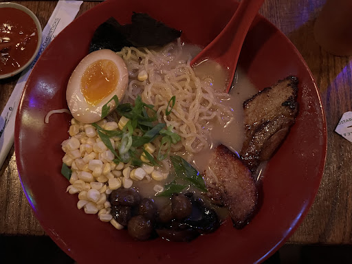 A red bowl of ramen with meat, eggs, vegetables, and noodles.