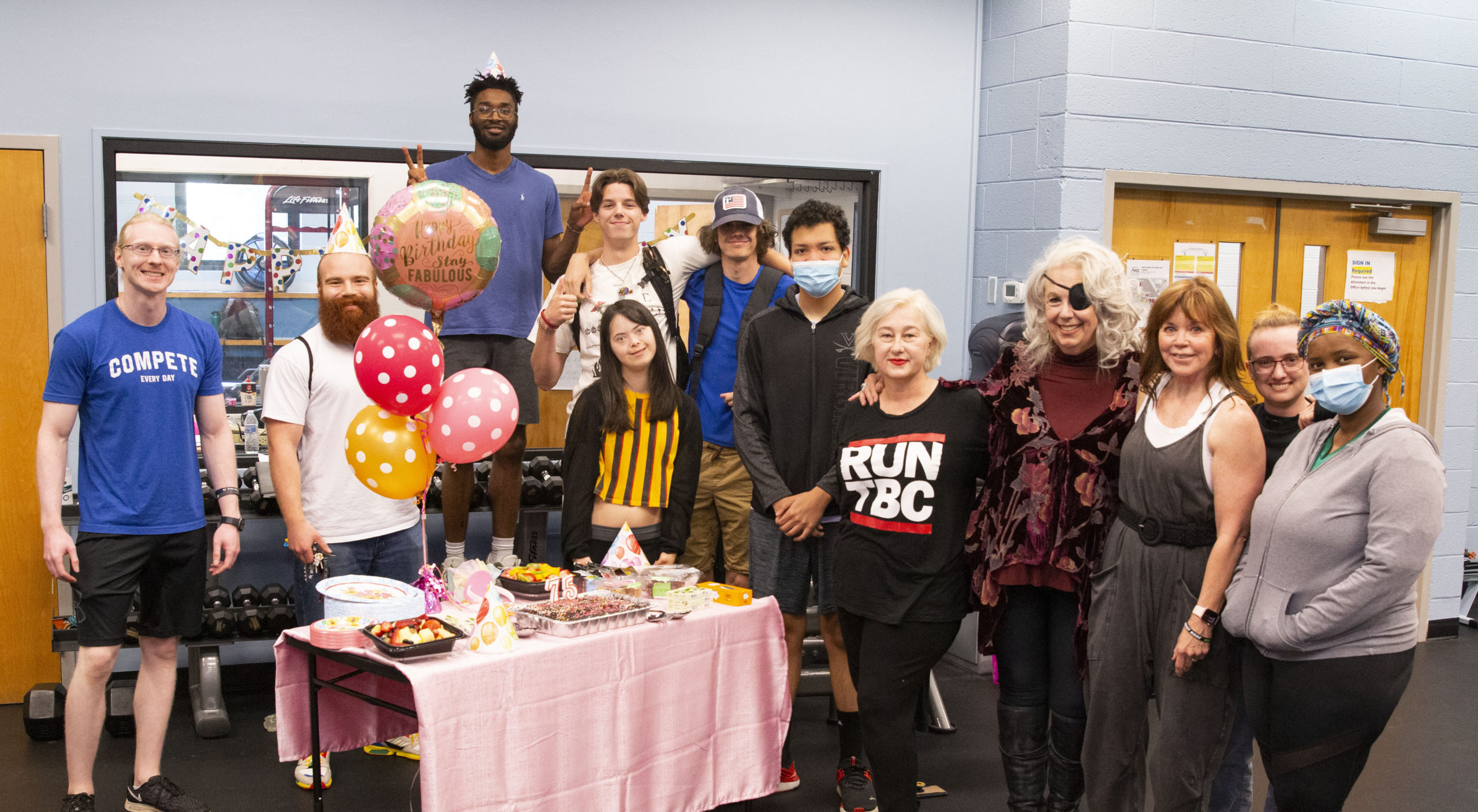 Students gather around a table with birthday cake and balloons.