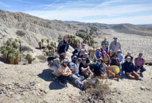 Students and faculty pose of the edge of a cliff overlooking an oasis