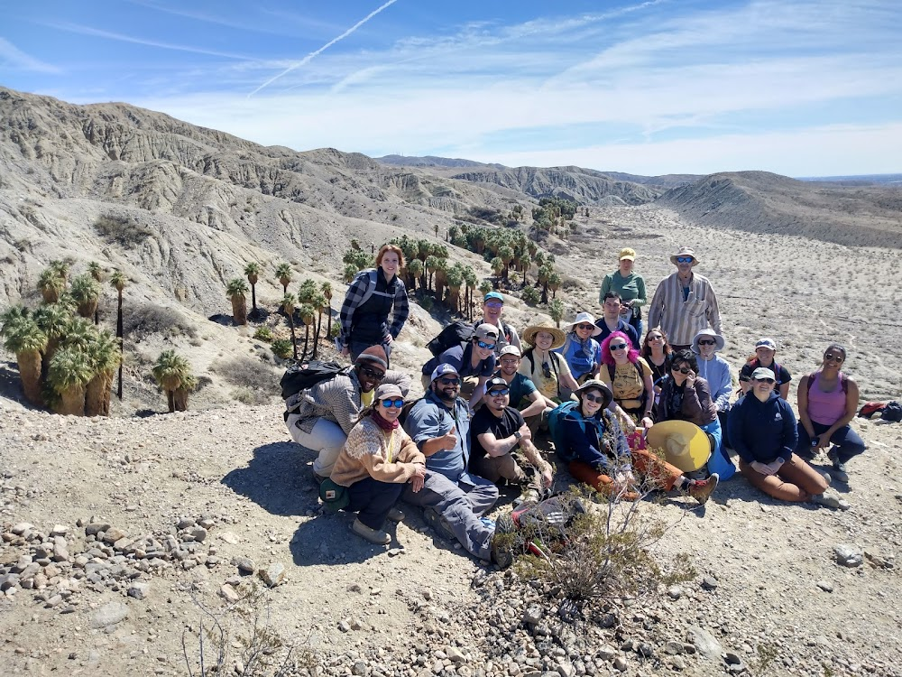 Students and faculty pose of the edge of a cliff overlooking an oasis