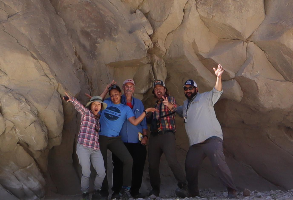 Faculty strike a goofy pose in front of a rock outcrop