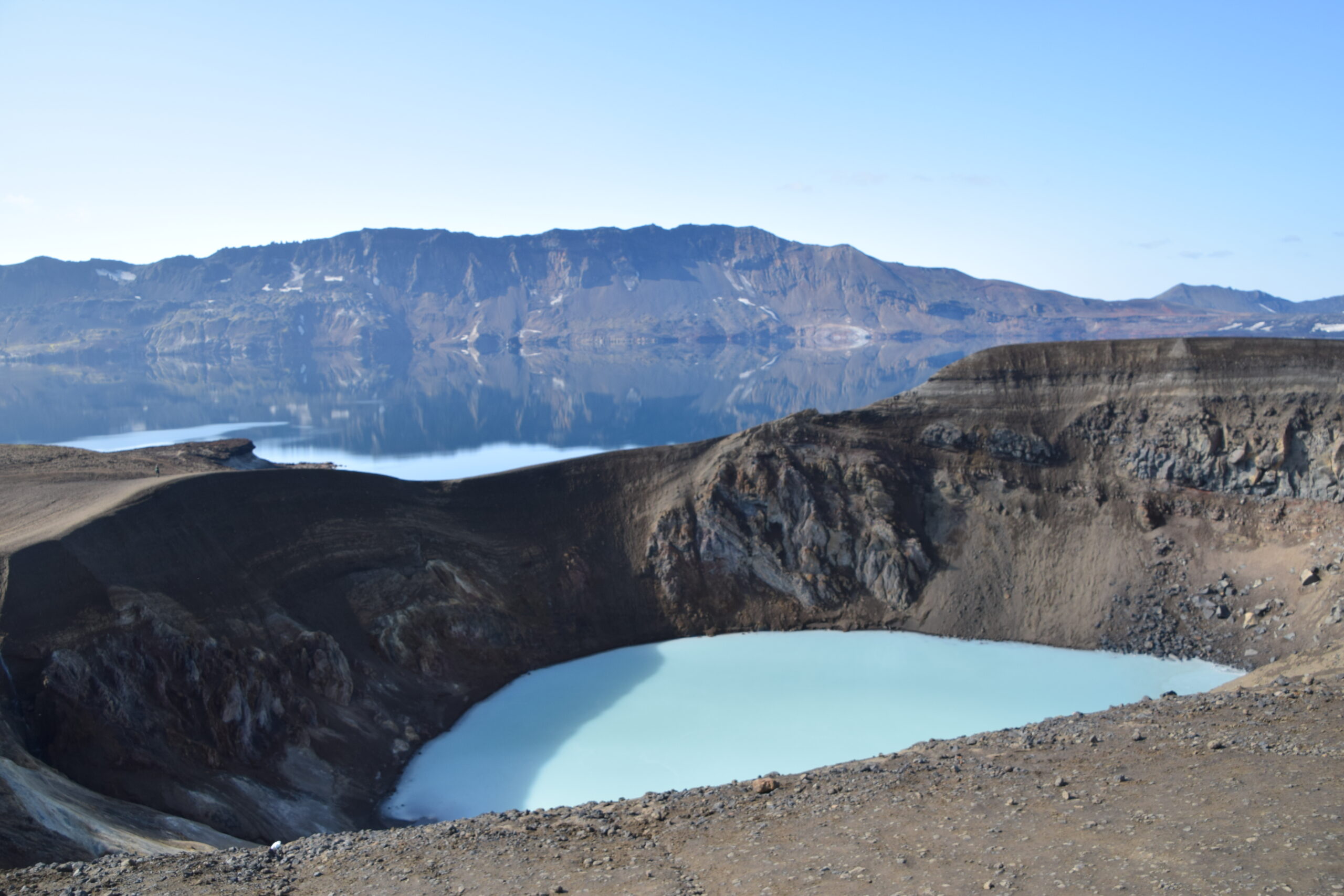 A light blue water basin below a brown and gray mountain/volcano