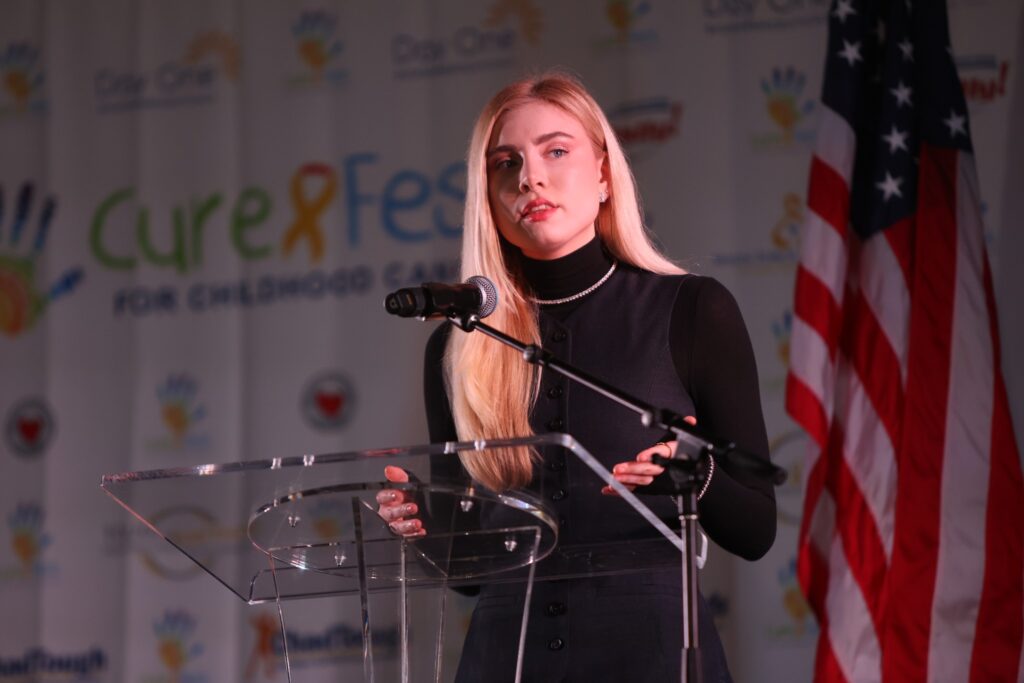 Curefest co-host Grace Wethor speaking in front of a Curefest banner.