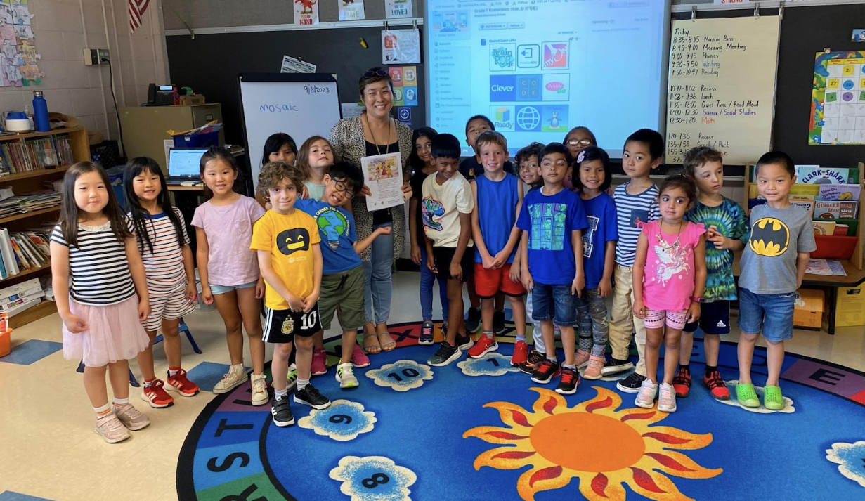 A teacher stands with her young students in her classroom, smiling at the camera