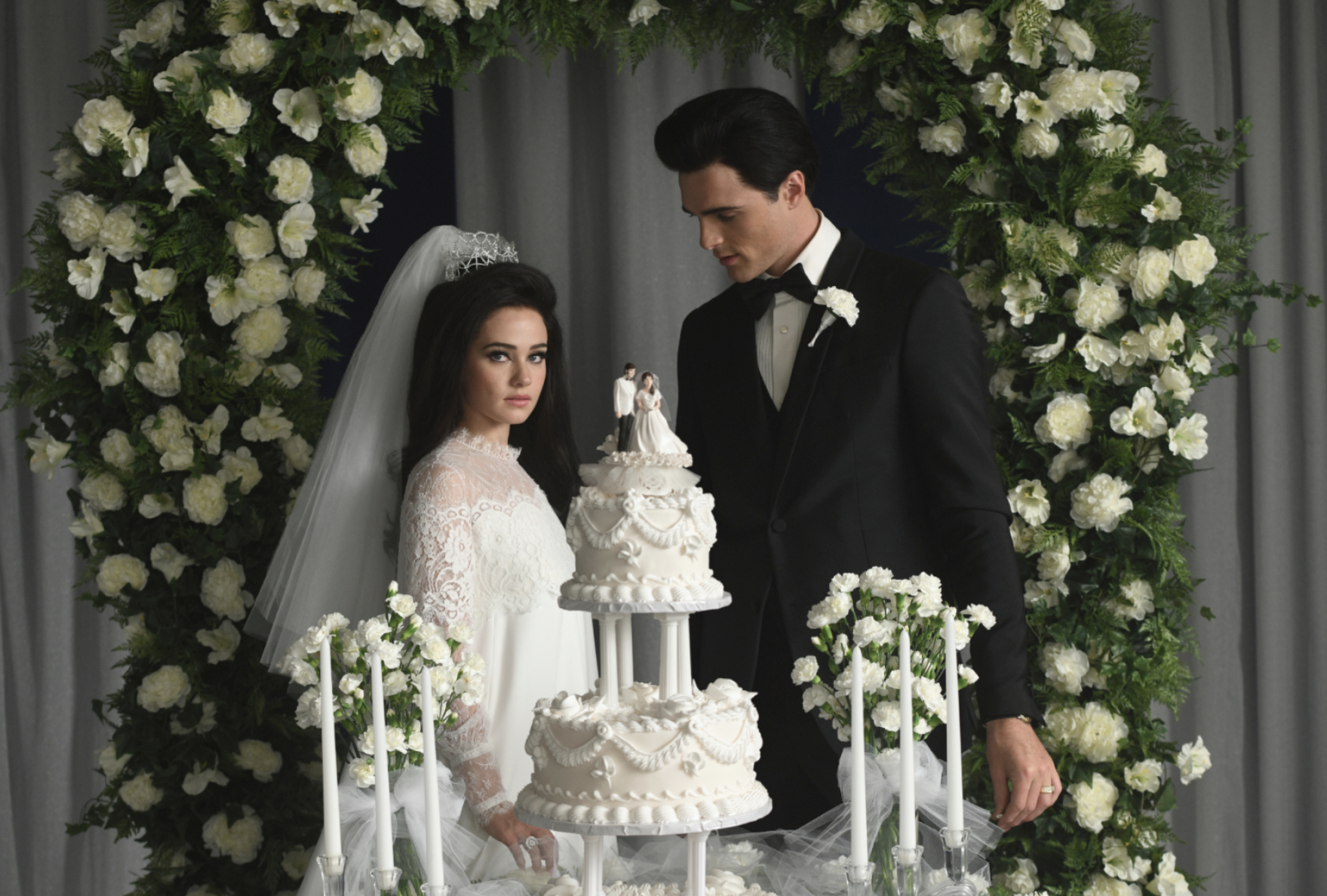 Jacob Elordi (Elvis) and Cailee Spaeny (Priscilla) stand behind a wedding cake.