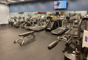 A variety of cardio machines, treadmills, stationary bikes, etc. against a wall with a tv on it.