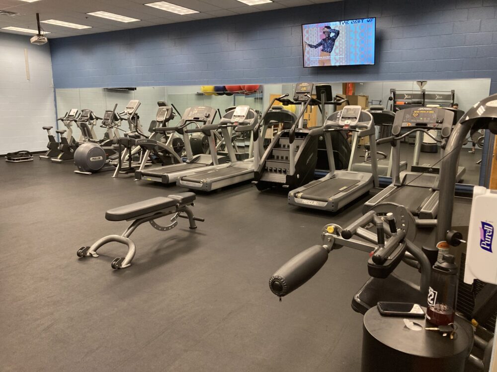 A variety of cardio machines, treadmills, stationary bikes, etc. against a wall with a tv on it.