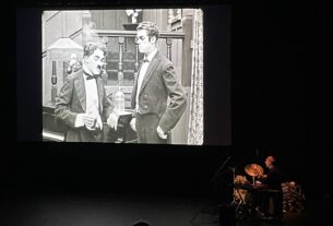 A screen showing "The Adventurer" with a man playing instruments to the bottom right of it.