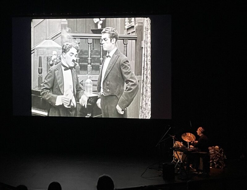 A screen showing "The Adventurer" with a man playing instruments to the bottom right of it.