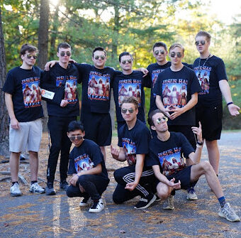 A group of male college students in sunglasses pose wearing black t-shirts that say "Jesus Has Rizzen"