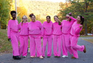 A group of female college students pose in bright pink sweat shirts and pants.
