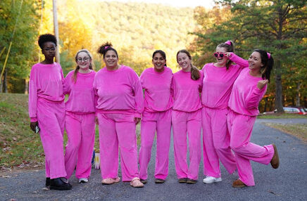 A group of female college students pose in bright pink sweat shirts and pants.