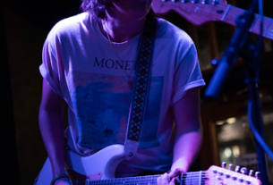A young man wearing a Monet t-shirt plays guitar on stage