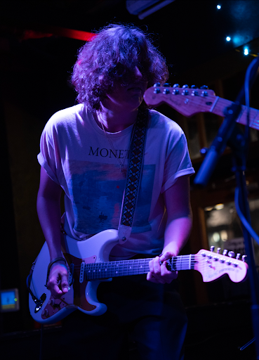 A young man wearing a Monet t-shirt plays guitar on stage