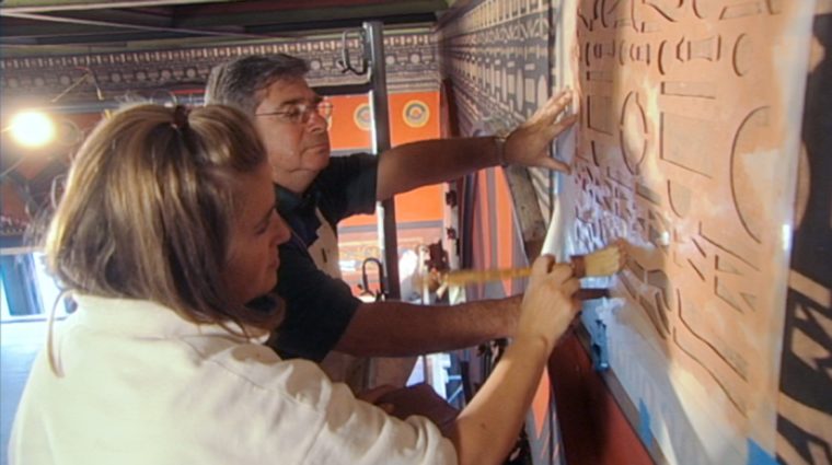A woman and her father paint through a template on a wall.