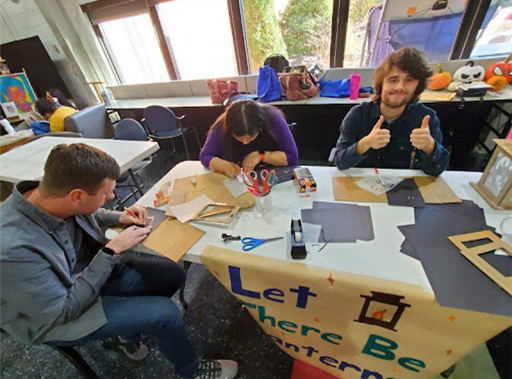 Three students sit at a table using paper and markers to make lanterns. 