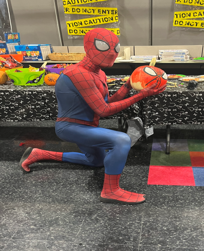 Someone in a Spiderman costume holding a Spiderman pumpkin