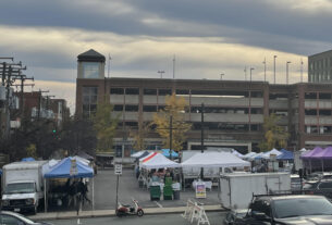 Tents for a farmers market in a parking lot in front of a brick parking garage