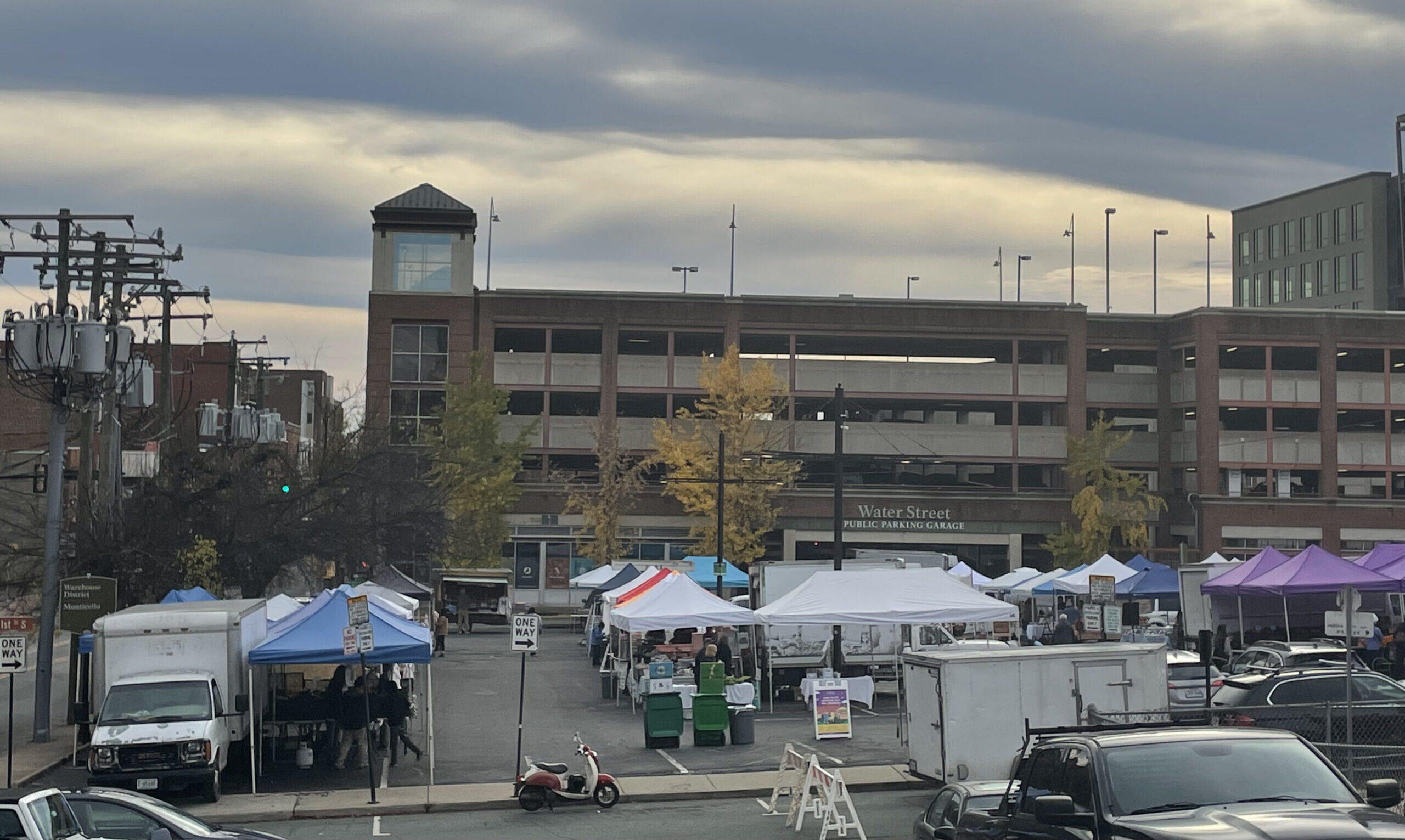 Tents for a farmers market in a parking lot in front of a brick parking garage