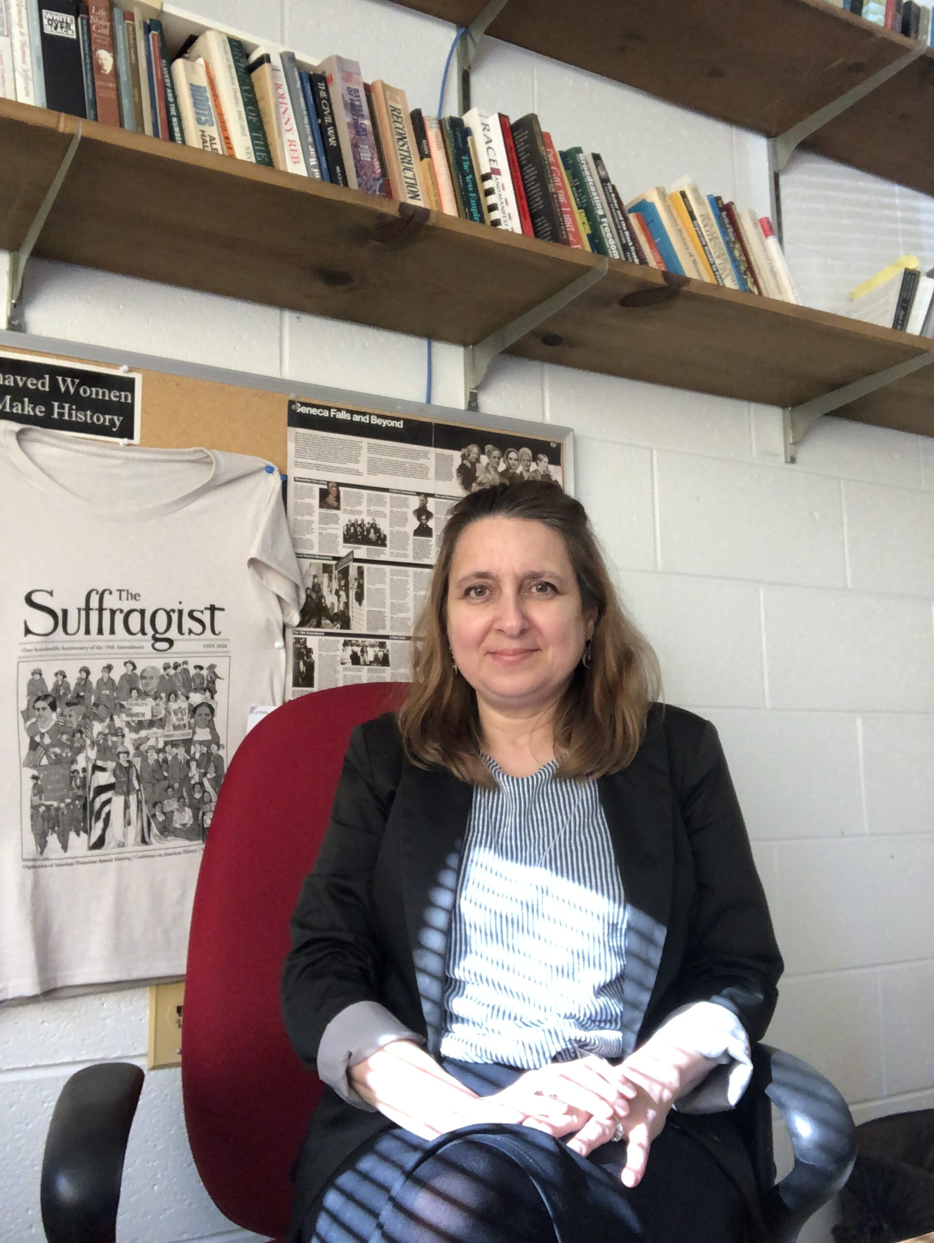 A picture of Jennifer Tomas sitting under a bookshelf.