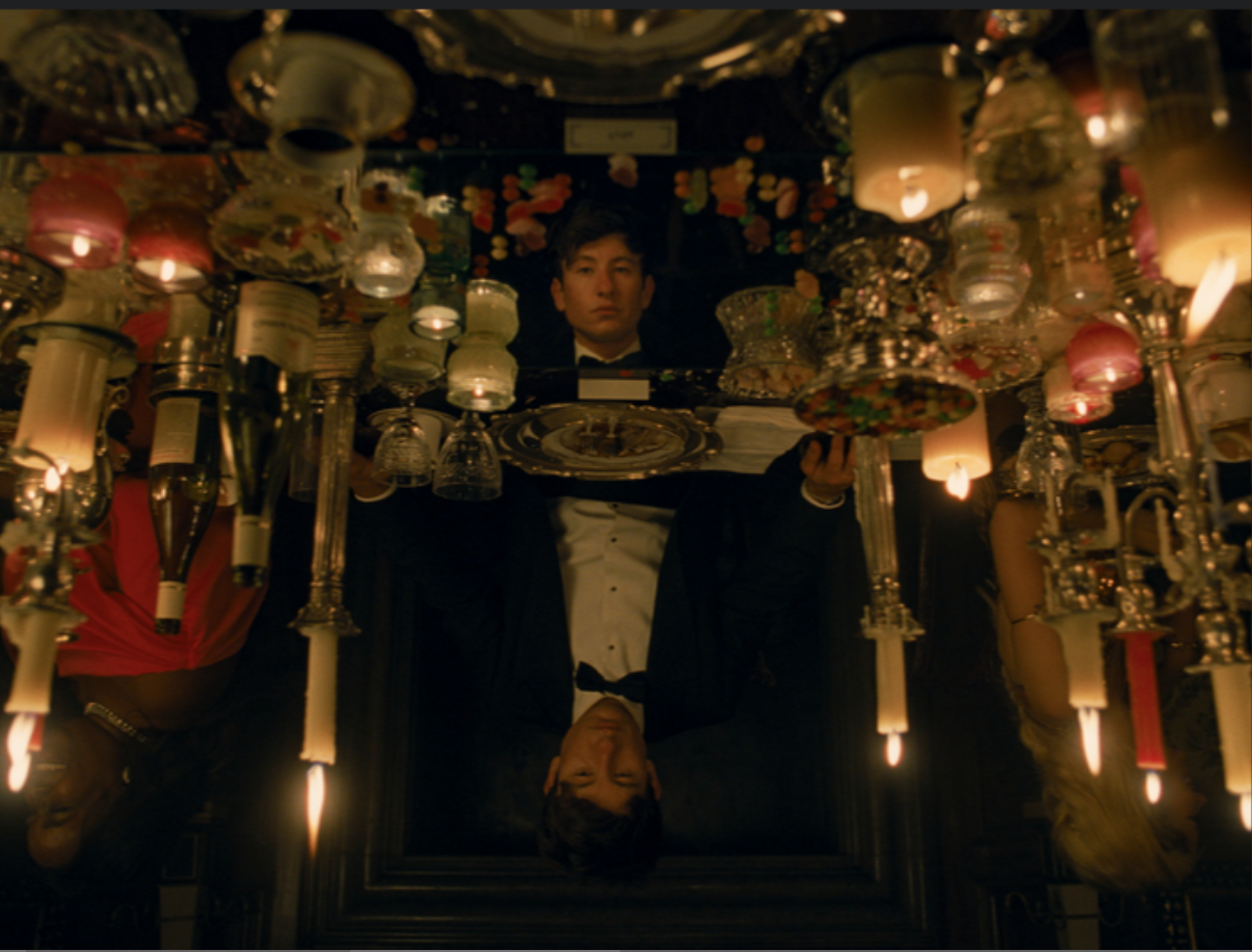 A man in a tuxedo sits at a table surrounded by candles. His reflection shows in the table.