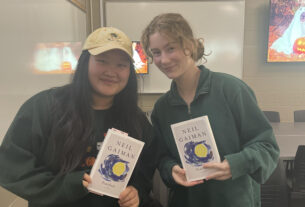 Two students in green sweatshirts pose with copies of Stardust, by Neil Gaiman.