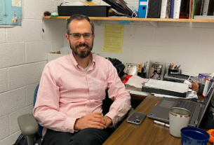 Dr. Zack Beamer sits in his office with bookshelves behind him