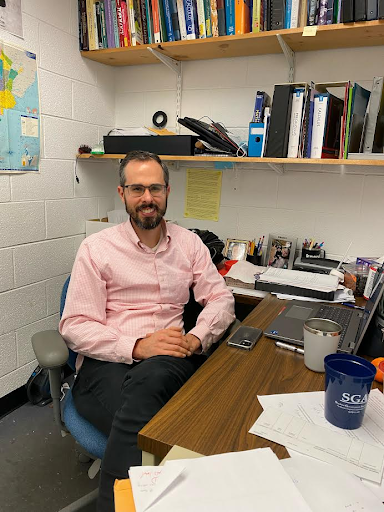 Dr. Zack Beamer sits in his office with bookshelves behind him