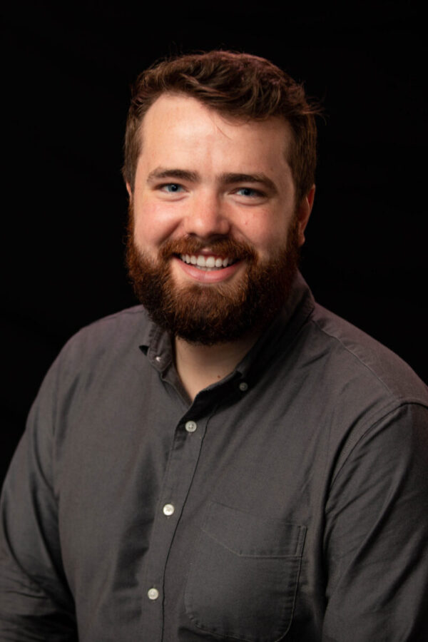 Adam Quinn smiles at the camera against a blank background