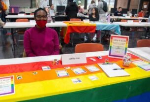 A student sits at a table with a rainbow flag on it at PVCC club day fair.