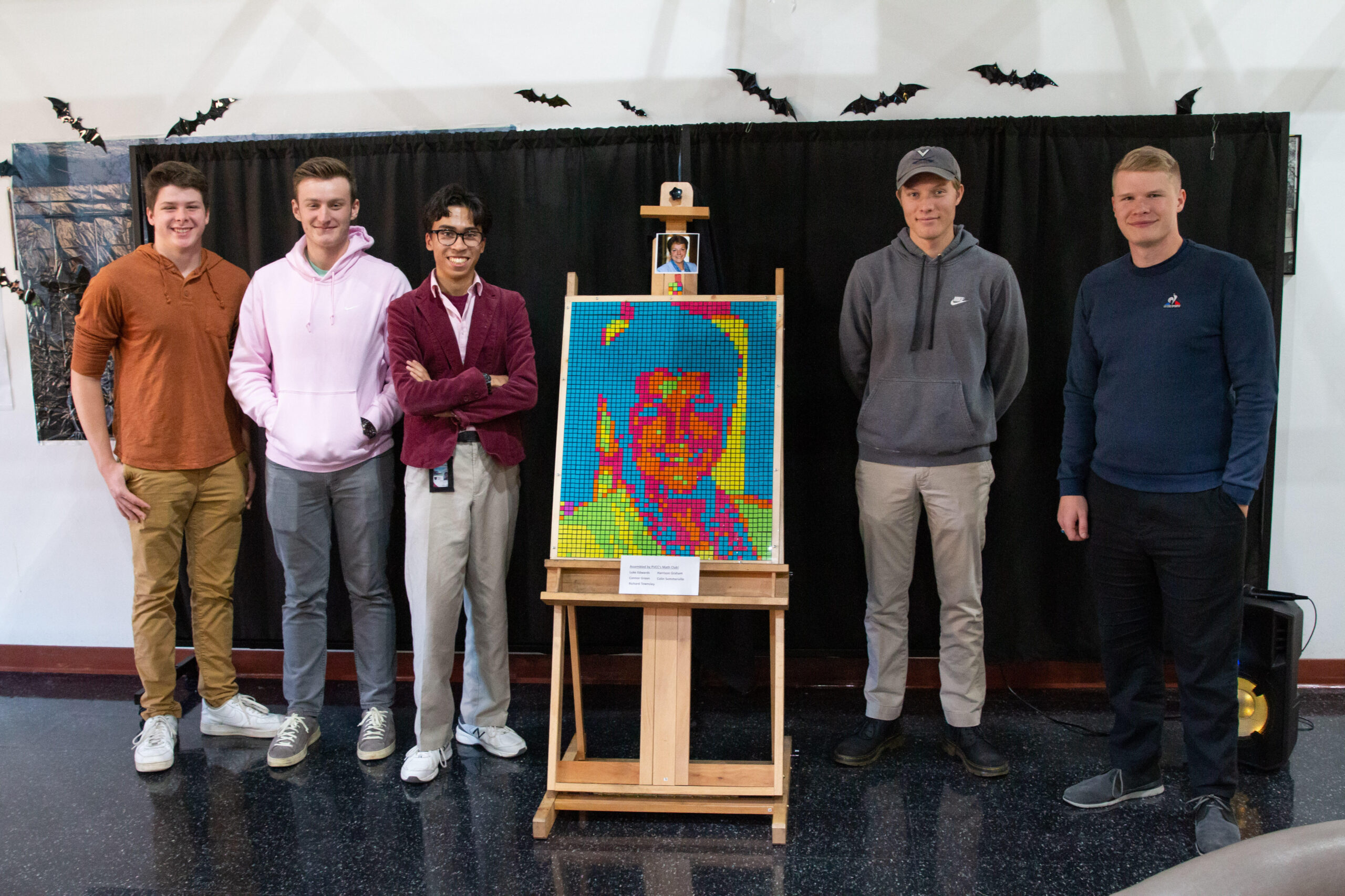 Members of the math club pose around the Rubik's cube portrait of Dr. Jean Runyon.