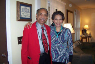 A man in a red jacket and Melody Day in a blue top smile for the camera