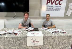 Club members Benjamin Marcus and Lidija Westfall wearing Forum shirts and handing out copies at the Forum's table.