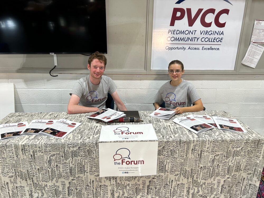 Club members Benjamin Marcus and Lidija Westfall wearing Forum shirts and handing out copies at the Forum's table.