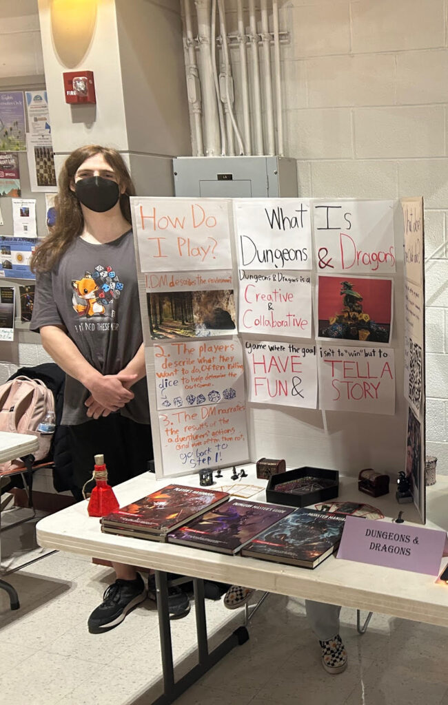 Three students surround the Dungeons and Dragons Club display table.